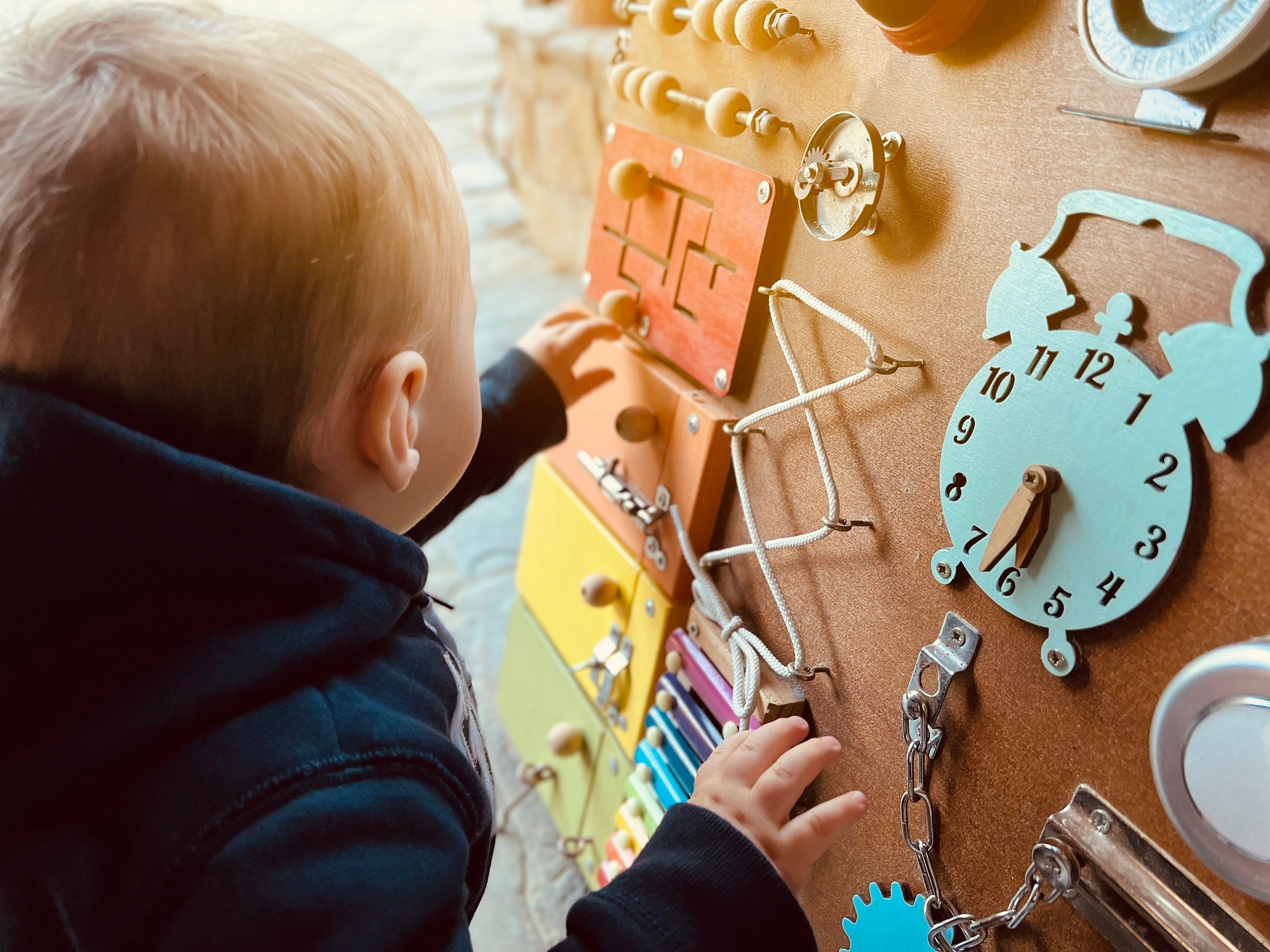 A little boy is playing with a busy board. Developming toy for children from one year old. Developming toy for children from one year old. Focus on the busy board