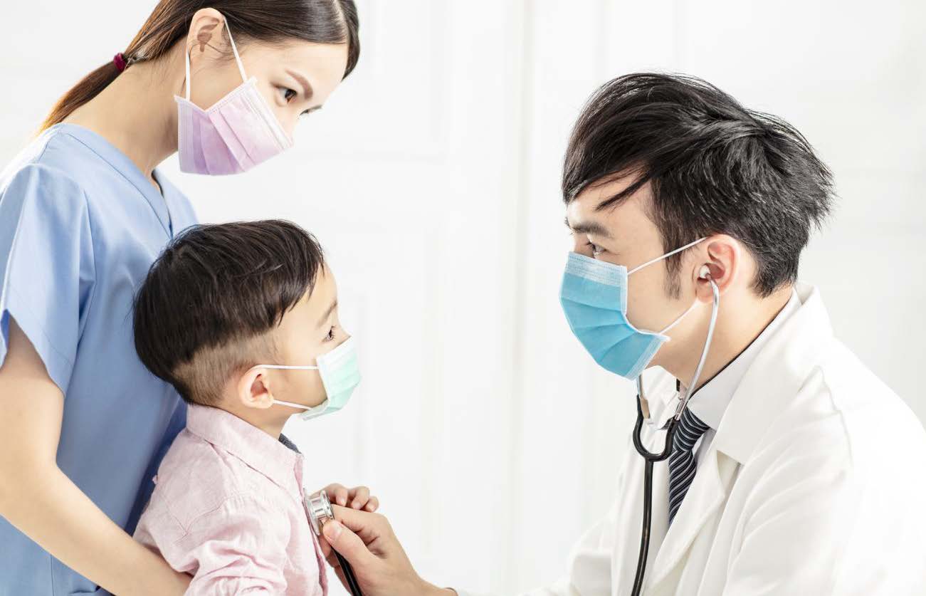 Doctor with an assistant using a stethoscope to check the heartbeat of a young boy.