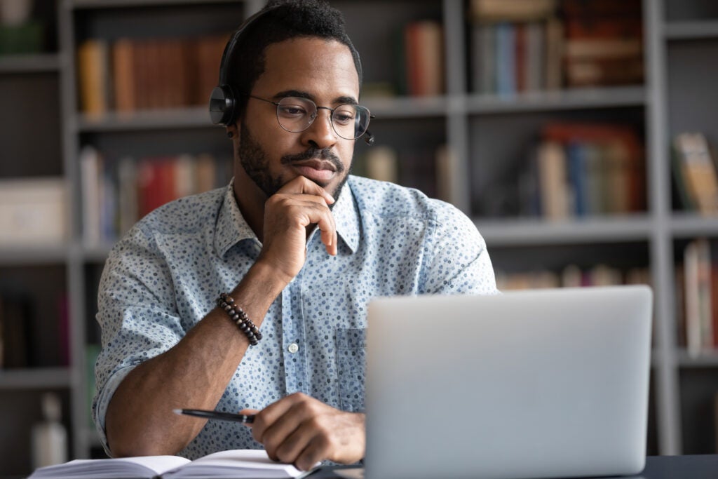 African guy wearing headset using internet on grey tablet in front of an open book