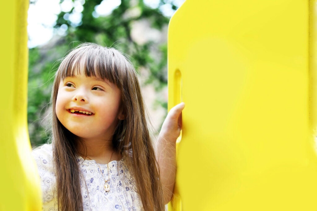 Portrait of beautiful young girl with downs syndrome on the playground in between two yellow partitions