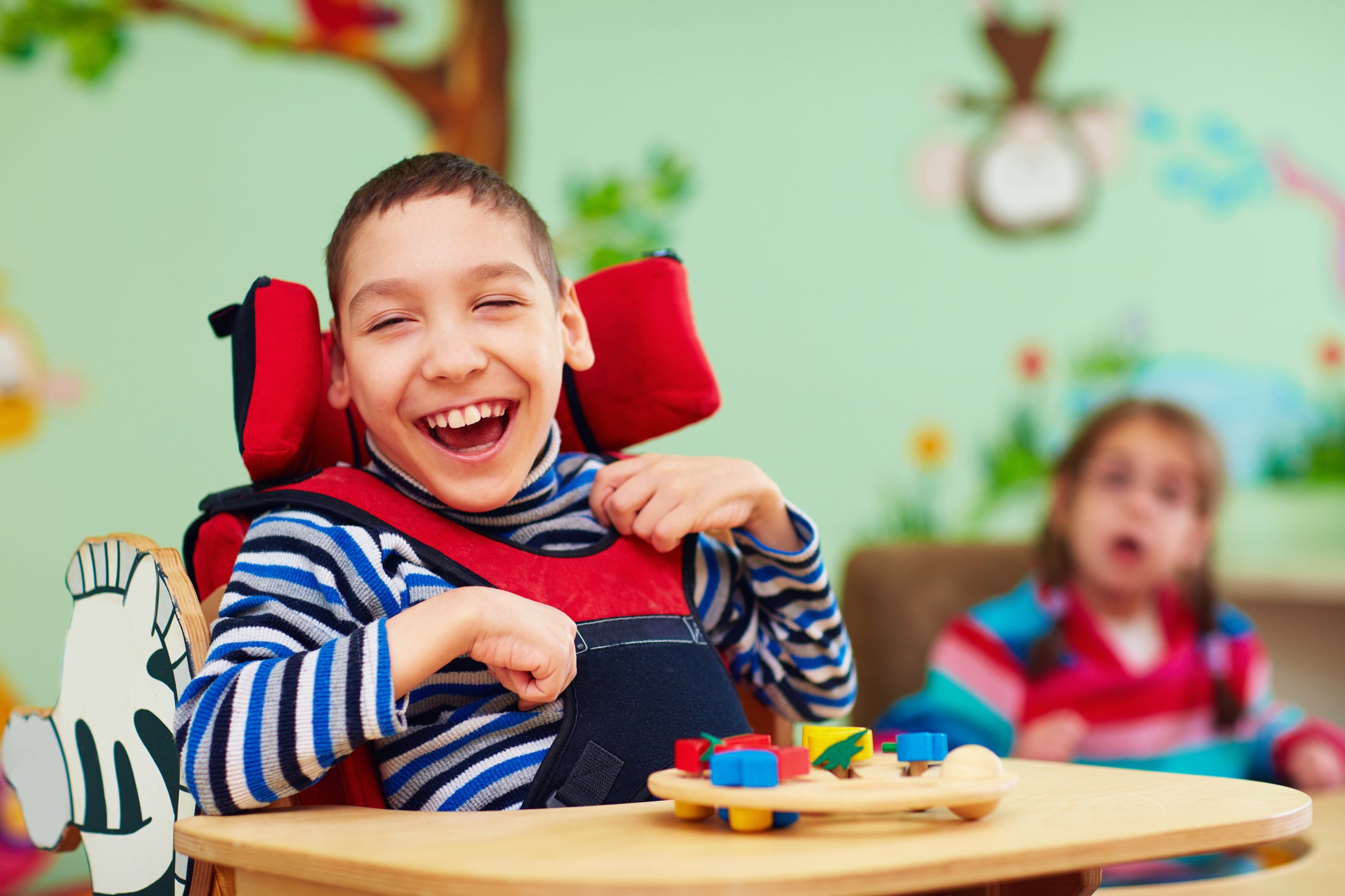 Cheerful, smiling boy sitting in high chair with colorful toys on tray