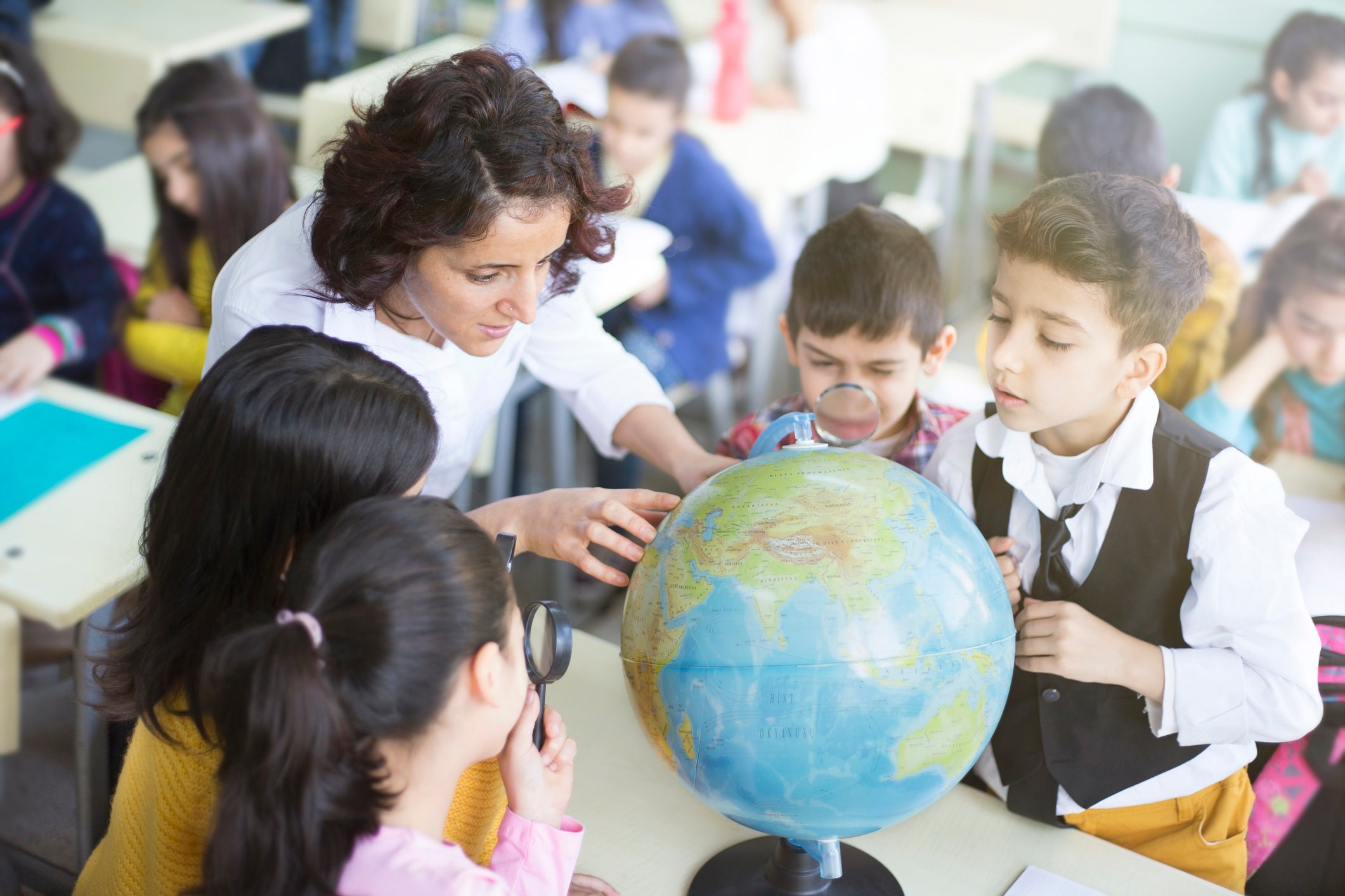 A female teacher and students looking at a globe with a magnifying glass in a classroom
