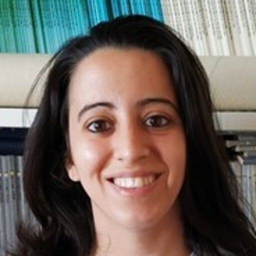 Olive skinned woman with shoulder length dark brown hair smiling in front of a bookshelf