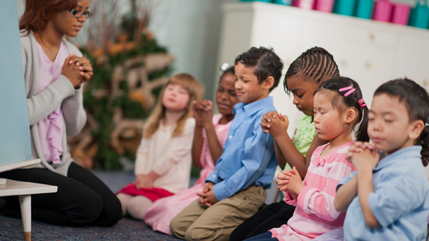 A group of children praying led by an adult